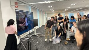 Employees observe a “Breaking News” segment on a big monitor during a workshop.