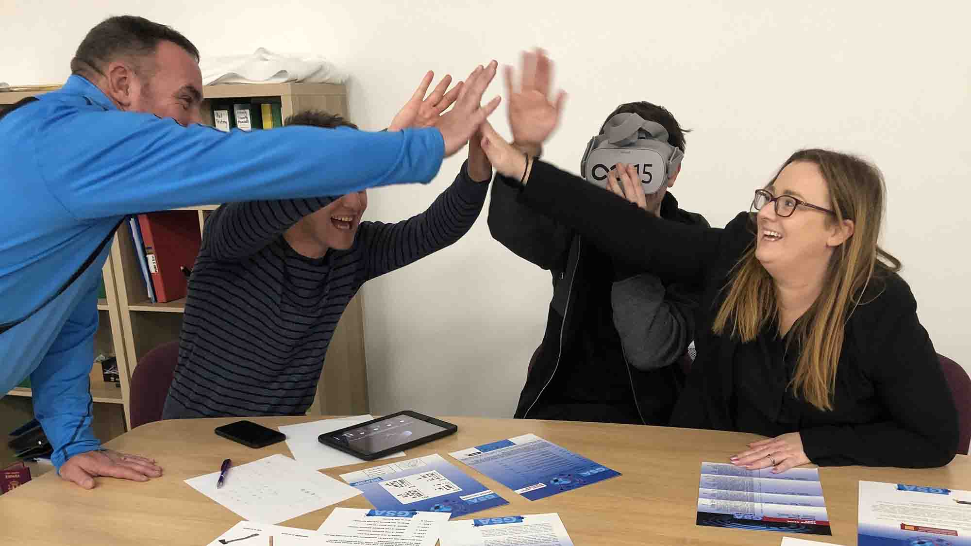 Excited teammates share a collective high-five over tablets and clue sheets at a table.