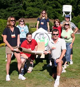 Group covers a cardboard vehicle with black plastic and orange ribbons in an outdoor build.