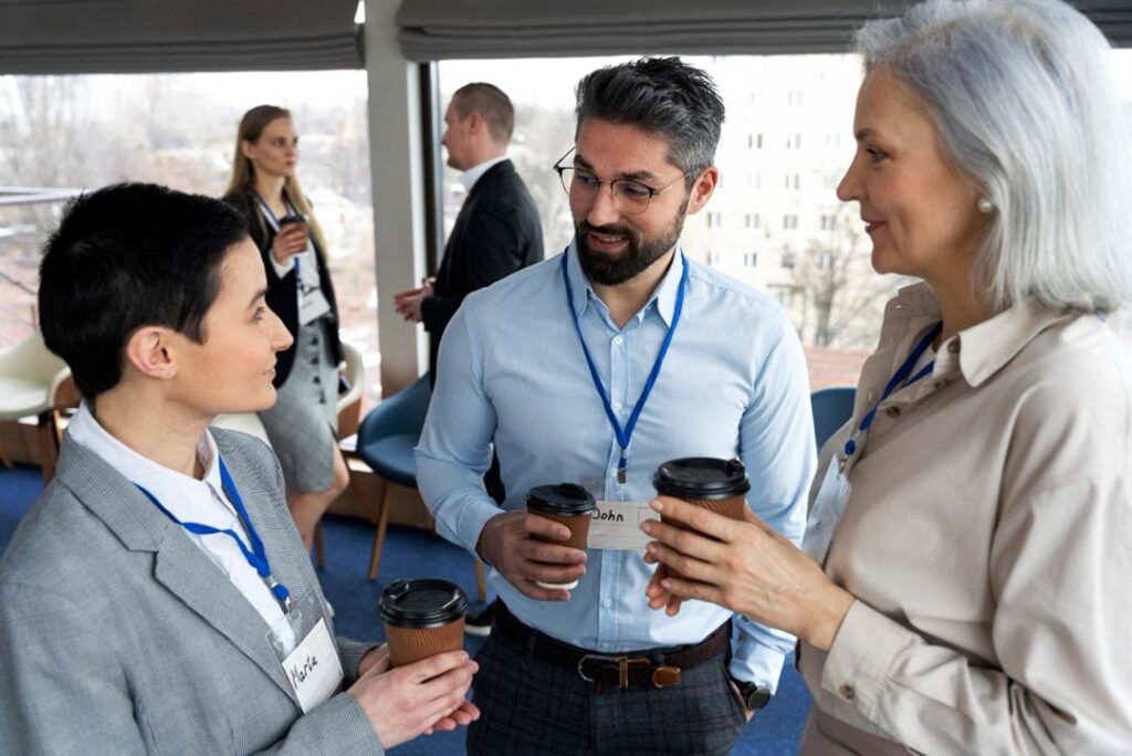 Three conference participants wearing name badges share coffee and conversation.