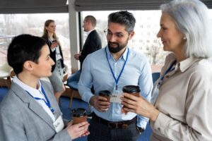 Three conference participants wearing name badges share coffee and conversation.