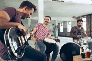 Trio of male musicians jam in a gritty studio with guitar, djembe and drums.