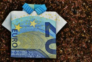 Ten-euro note folded into an origami shirt on a speckled background.